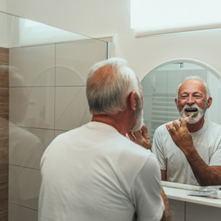 An older man brushing his teeth in front of a bathroom mirror