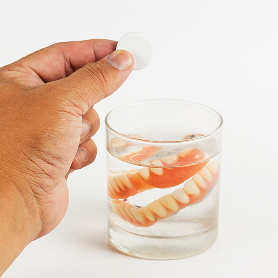 Person cleaning their dentures in a glass of water