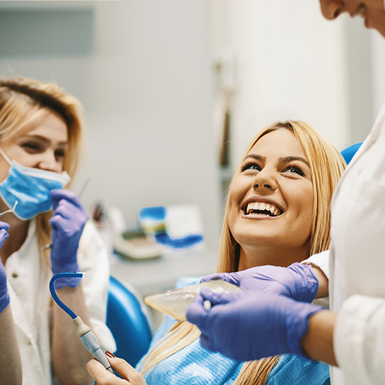 Woman in dental chair grinning up at her dentist