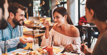 Group of smiling friends eating meal at restaurant