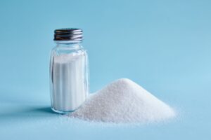 Jar of salt next to a pile on a light blue background