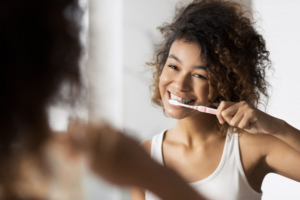 Young woman smiling in mirror as she brushes her teeth