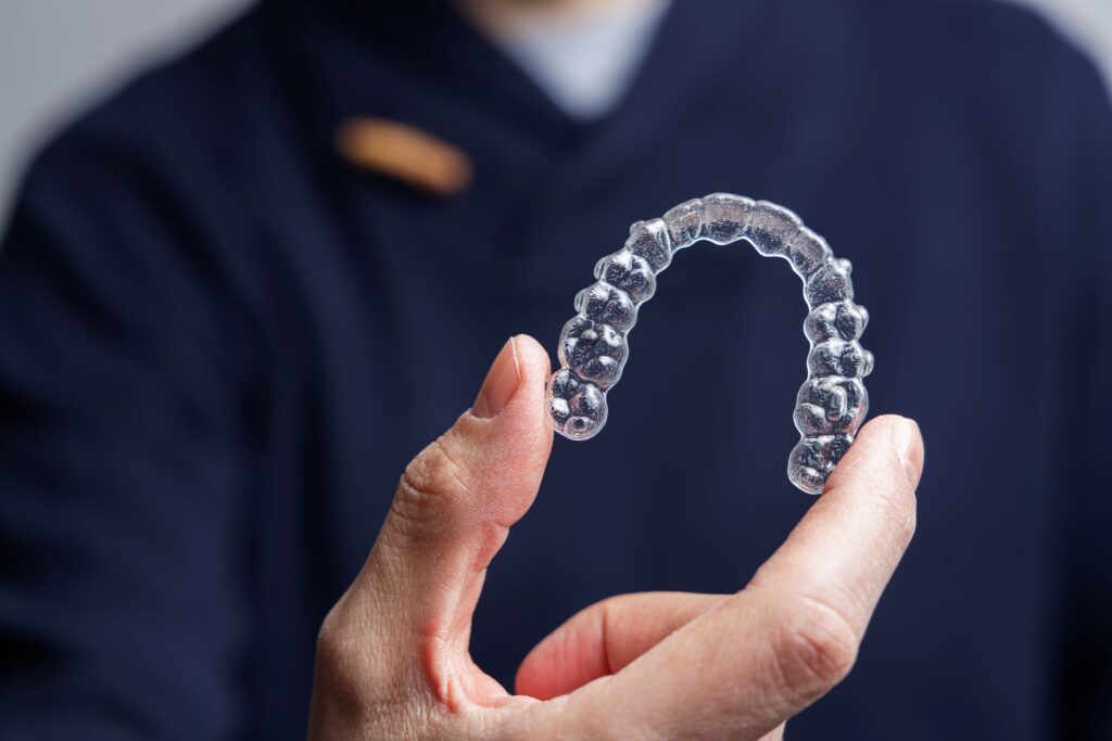 Dentist in dark blue scrubs holding Invisalign with thumb and forefinger